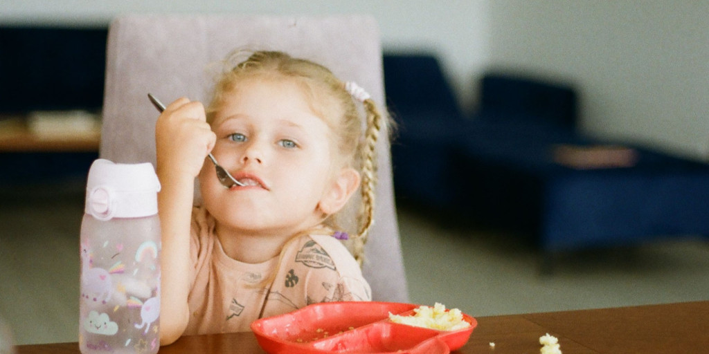 Photograph of a young girl sitting at a table, eating