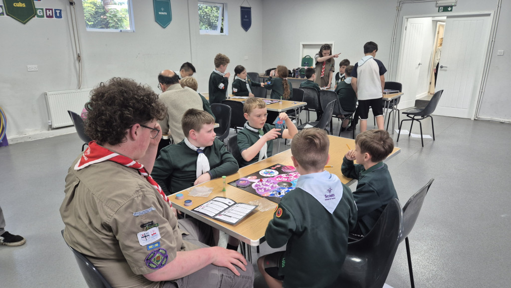 Groups of young Cubs sit around three tables playing boardgames
