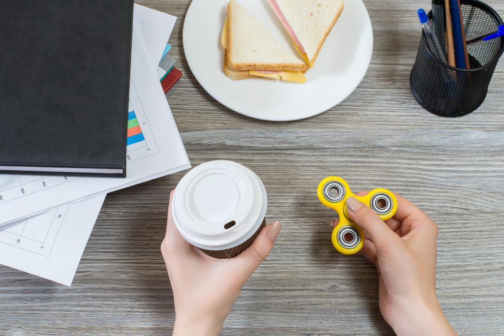 A person holding a coffee cup in one hand and a fidget spinner on the other hand
