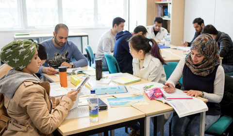 Photograph of people gathered around tables in a community discussion setting, sharing information and exploring practical solutions to financial challenges, community support and improving wellbeing