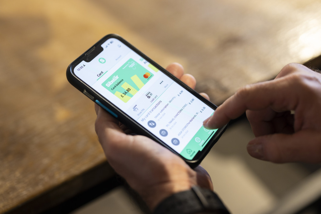 Close-up photograph of a person using a mobile banking app on a smartphone to check account balances and transactions, illustrating budgeting, money management and financial decision-making.