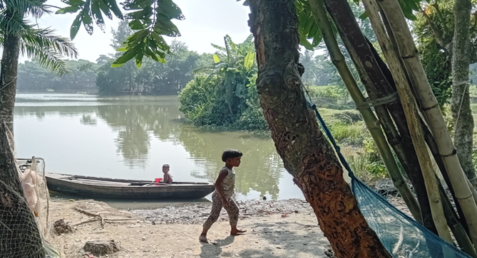 Photograph of a child walking by a lake in rural Bangladesh with a person in a boat in the background.