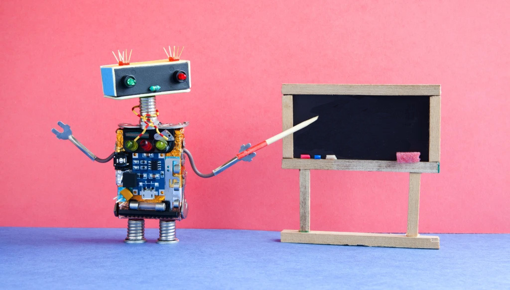 A robot made out of different materials using a pointer at a small chalkboard