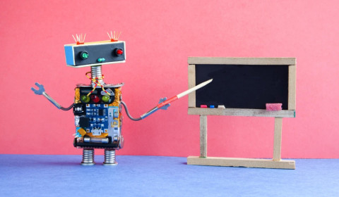 A robot made out of different materials using a pointer at a small chalkboard