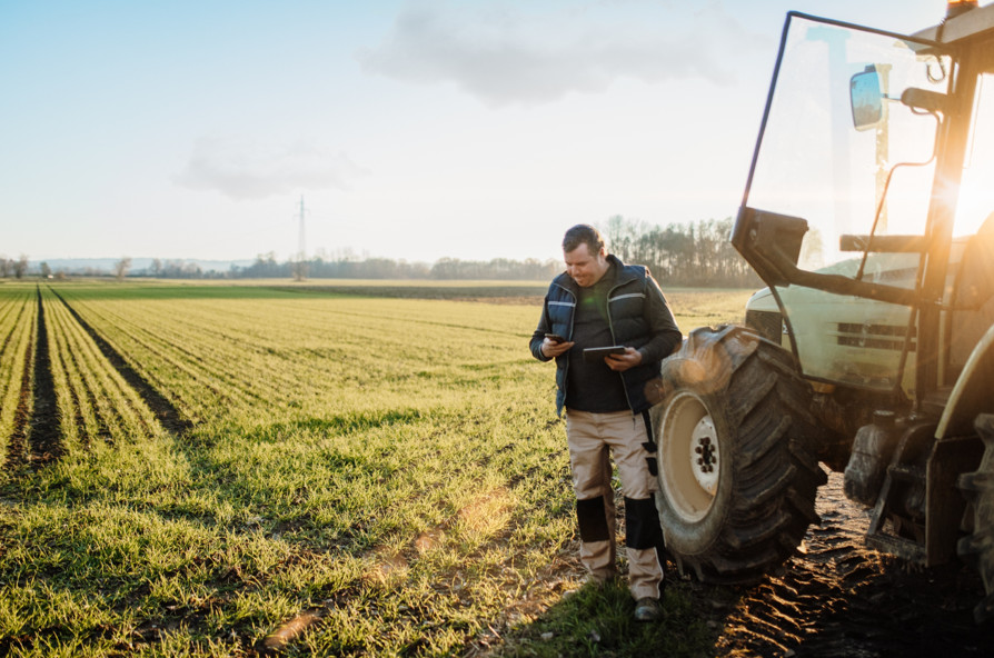 Person standing beside a tractor in a rural field, representing the experiences and challenges faced by people living in rural communities