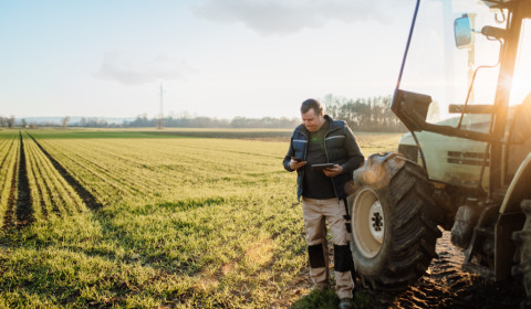 Person standing beside a tractor in a rural field, representing the experiences and challenges faced by people living in rural communities