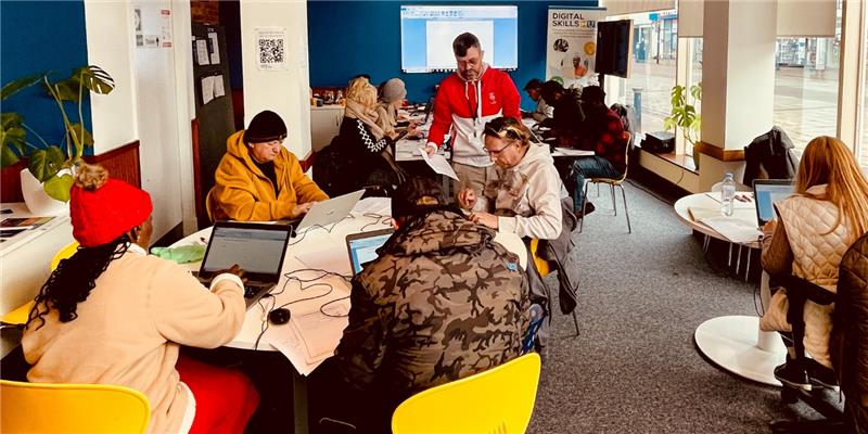 Photograph of a group of people working on laptops in a bright room with blue walls.