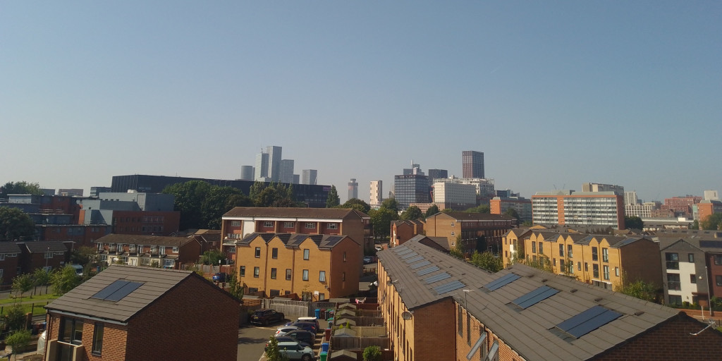 Photograph of Ardwick. There are houses in the foreground and Manchester's skyline in the background.