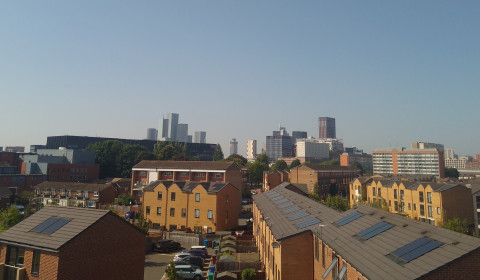 Photograph of Ardwick. There are houses in the foreground and Manchester's skyline in the background.