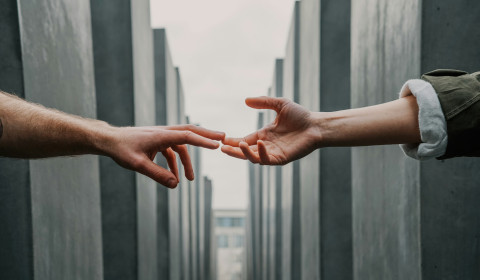 two hands reach out to each other, fingertips just making contact, reminiscent of 'The Creation of Adam' painting by Michelangelo, set against a stark background of concrete structures