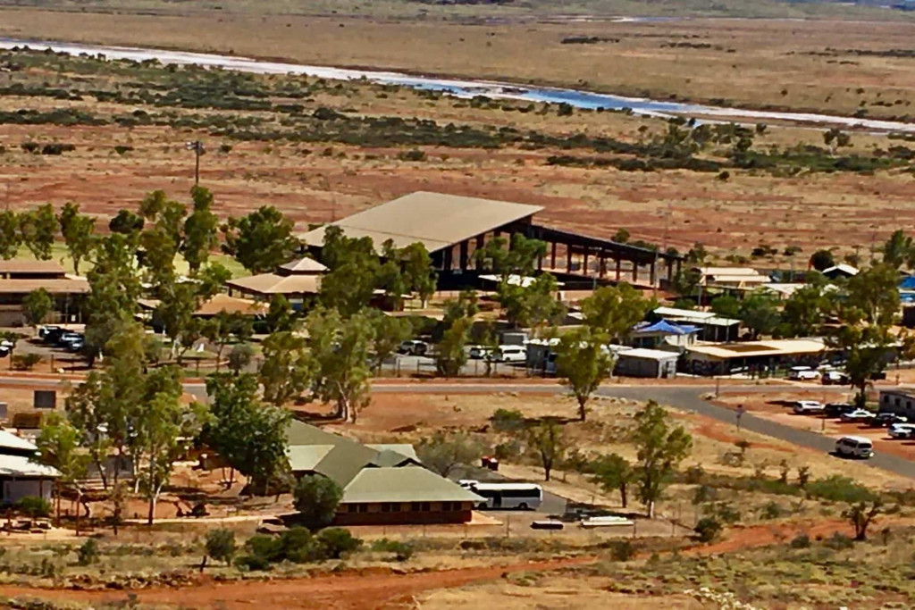 Aerial view of terracota coloured buildings, with trees and vehicles, and a river in the background.