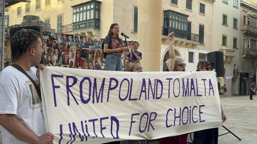 A group of people in a street hold a banner reading