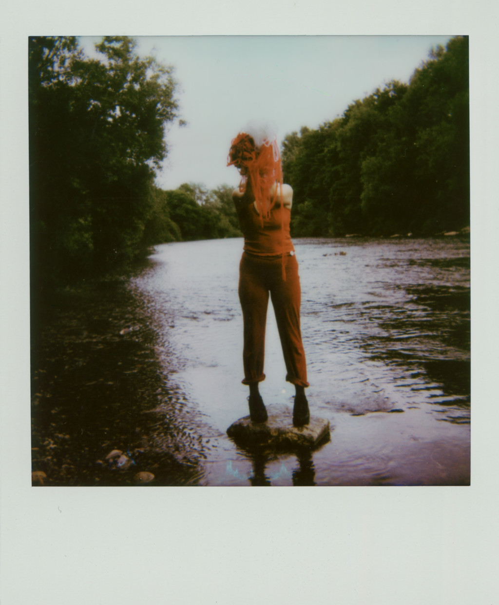 Person standing on a stone in the middle of a lake with a splash of paint over their face