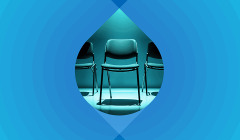 Photograph of a row of office chairs on a blue background. One chair is in a spotlight.
