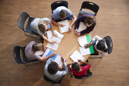 A photograph of young people sitting round a table, writing. The photograph is taken from above