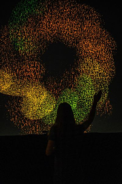 Swirling doughnut shape made up of many dots, in green, orange and yellow