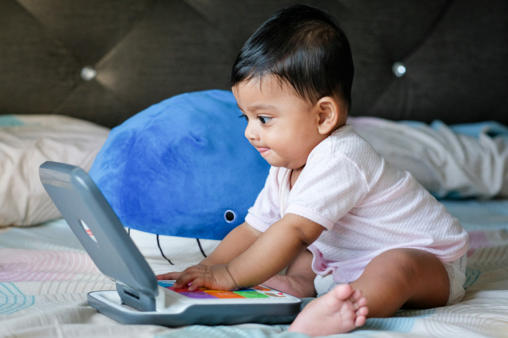A baby playing with a toy laptop, with a look of intense concentration. Credit to Mahmud Ahsan on Unsplash.