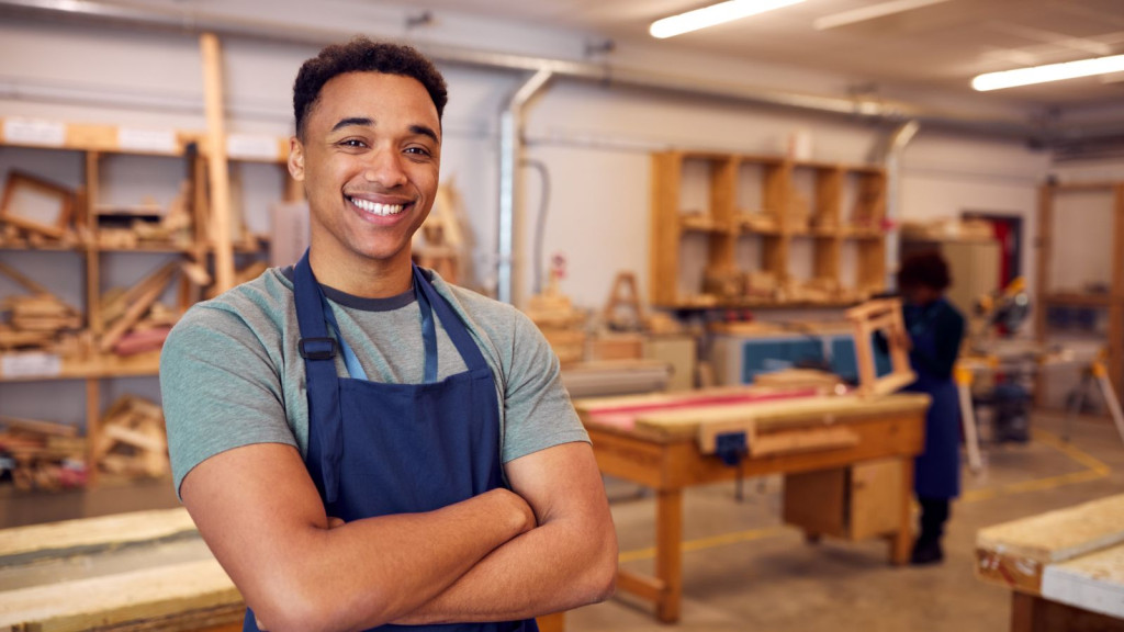 Man smiling with arms folded stood in a woodwork workshop
