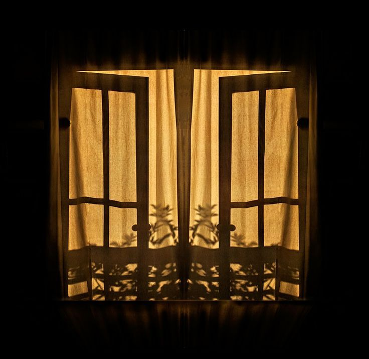Windows seen from the outside, with golden light coming through the curtains.