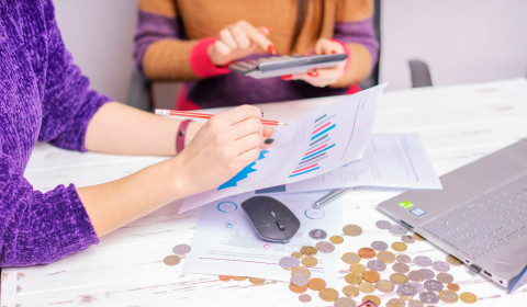 Two women reviewing financial documents and money together at a desk.