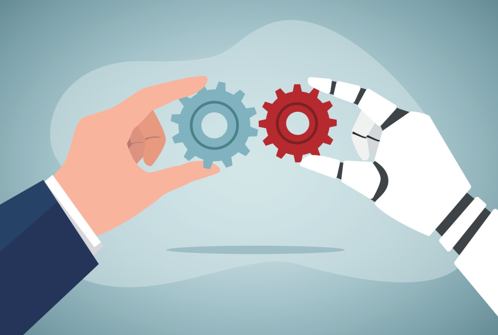 A human hand and robot hand holding two different cogs together being red and blue.