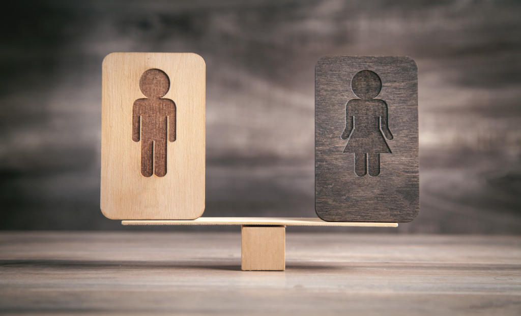A set of scales with a balancing object on either side, one with a male figure symbol on it, one with a female figure symbol on it and on this one the colour has faded into the background.