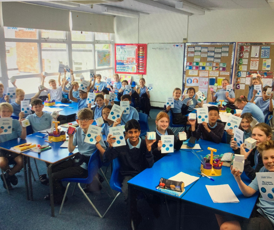 Photo of school children in a classroom looking at the camera and holding up diplomas