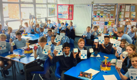 Photo of school children in a classroom looking at the camera and holding up diplomas
