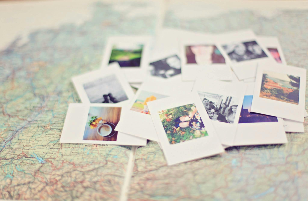 A pile of around 15 polaroid pictures scattered on top of a map. The pictures range from landscapes to coffee cups to selfies.