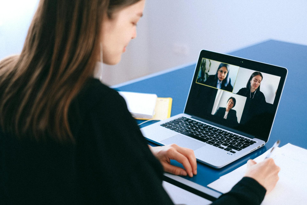 An image of a girl on a video call with three other team members. She is holding a pen to paper.