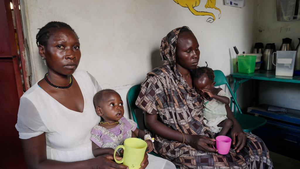 Two mothers sit in their kitchen with very young children on their laps