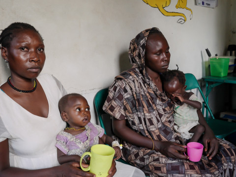Two mothers sit in their kitchen with very young children on their laps