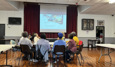 Photo of participants at an event sitting in a circle in front of a presentation screen