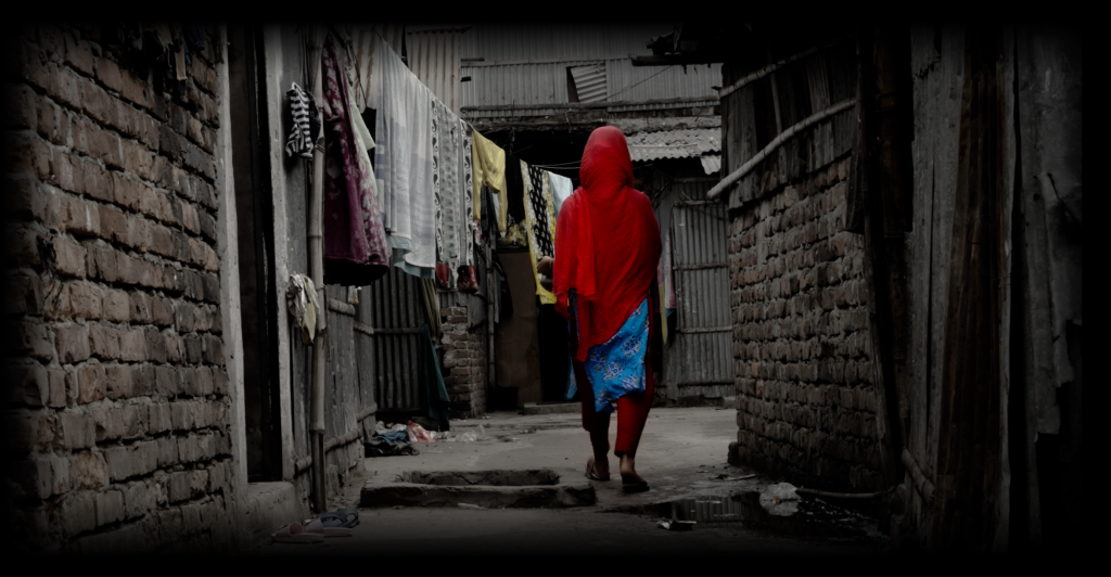 A community member walks through a small path between house, past a washing line