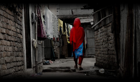 A community member walks through a small path between house, past a washing line
