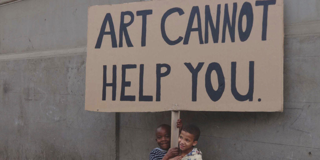 Two small kids carrying a cardboard sign which says 'Art cannot help you'