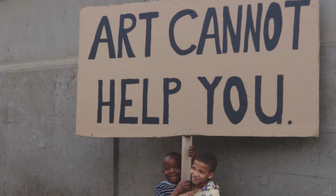 Two small kids carrying a cardboard sign which says 'Art cannot help you'