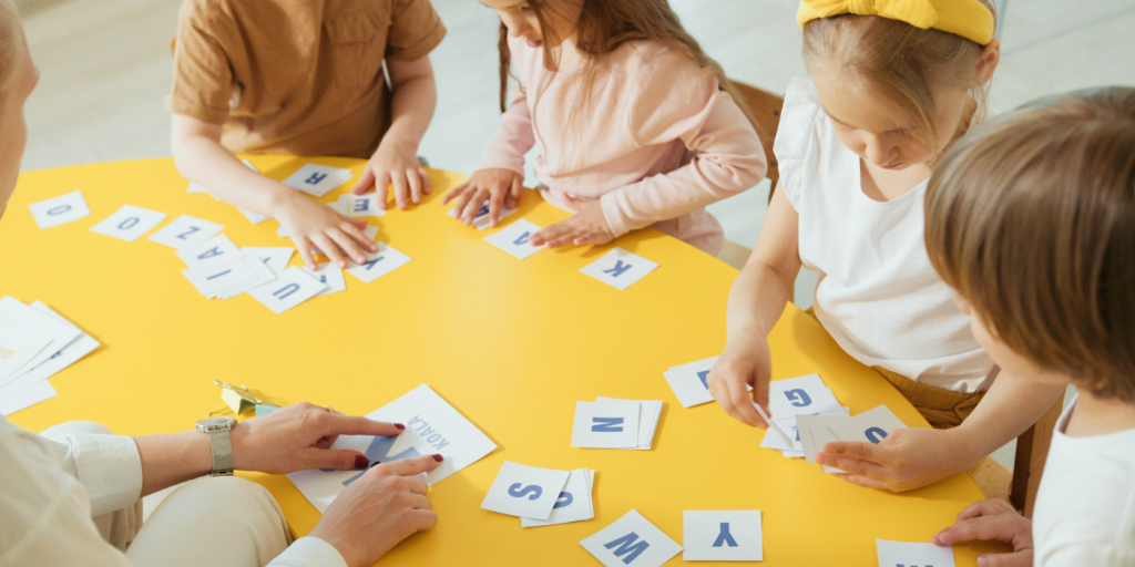 Kids playing with cards with letters on them at a yellow table
