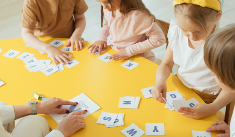Kids playing with cards with letters on them at a yellow table