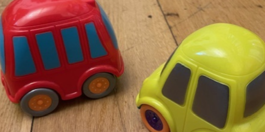 Two small toy cars, one red and one yellow, sitting on a wooden floor