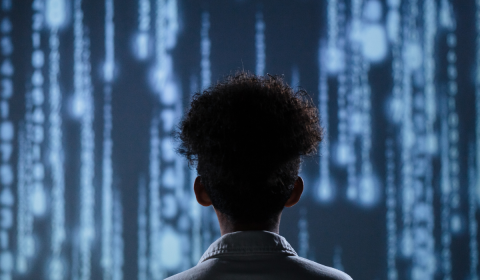 Silhouette of the back of someone's head who is standing in front of a screen with futuristic IT images on it