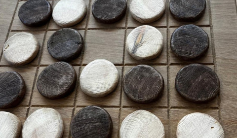 Photograph of a wooden draughts board with black and white circular counters on it