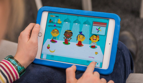 A child is playing an iPad game, sharing food between characters.