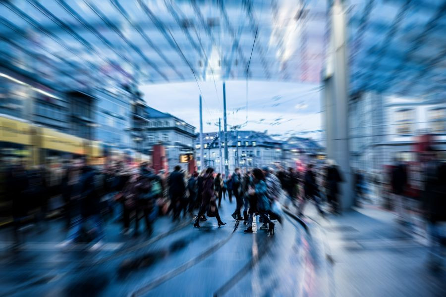 A blurred city scene shows crowds crossing tram tracks, capturing the fast pace and energy of urban life.