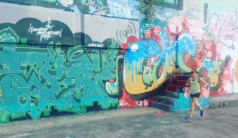 Photograph of a woman dressed in workout clothing running past a wall covered in graffiti