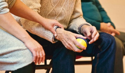 A younger lady lays her hand on an older gentleman's arm who is holding a ball in a caring way