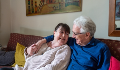 An older couple hug on a sofa