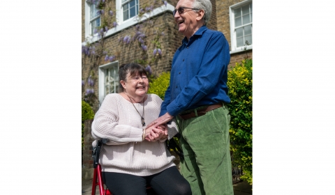 Older women in a wheel chair with male carer holding hand