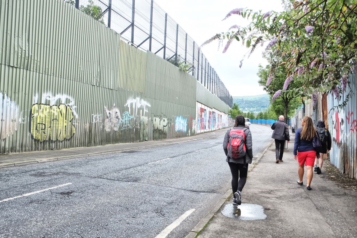 Group of people walking past the graffiti peace walls of Belfast.