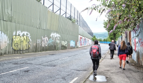 Group of people walking past the graffiti peace walls of Belfast.